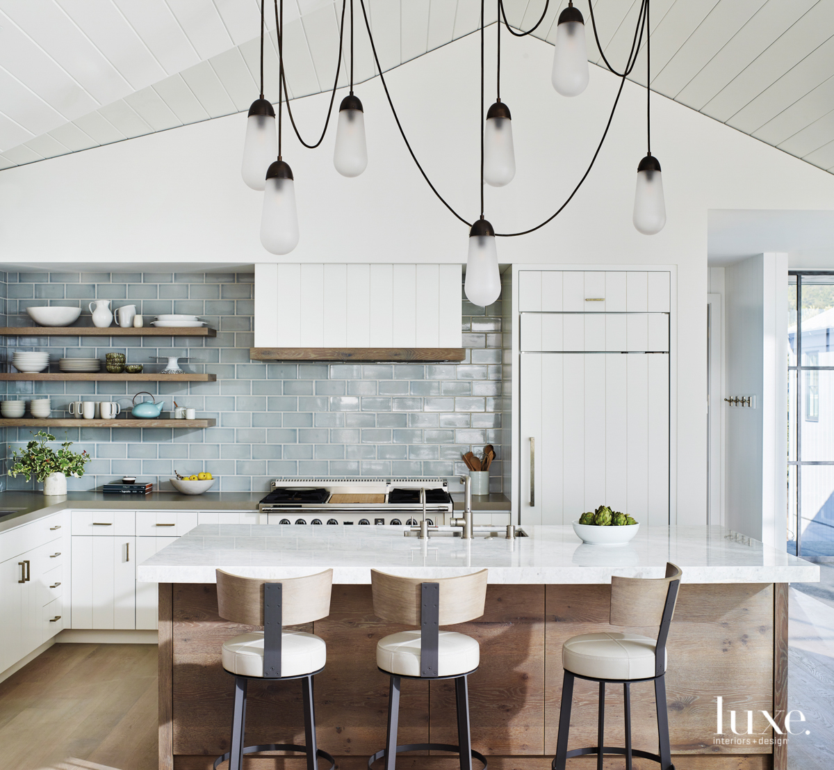 A kitchen is accented with sea-blue tile and a sculptural light fixture.