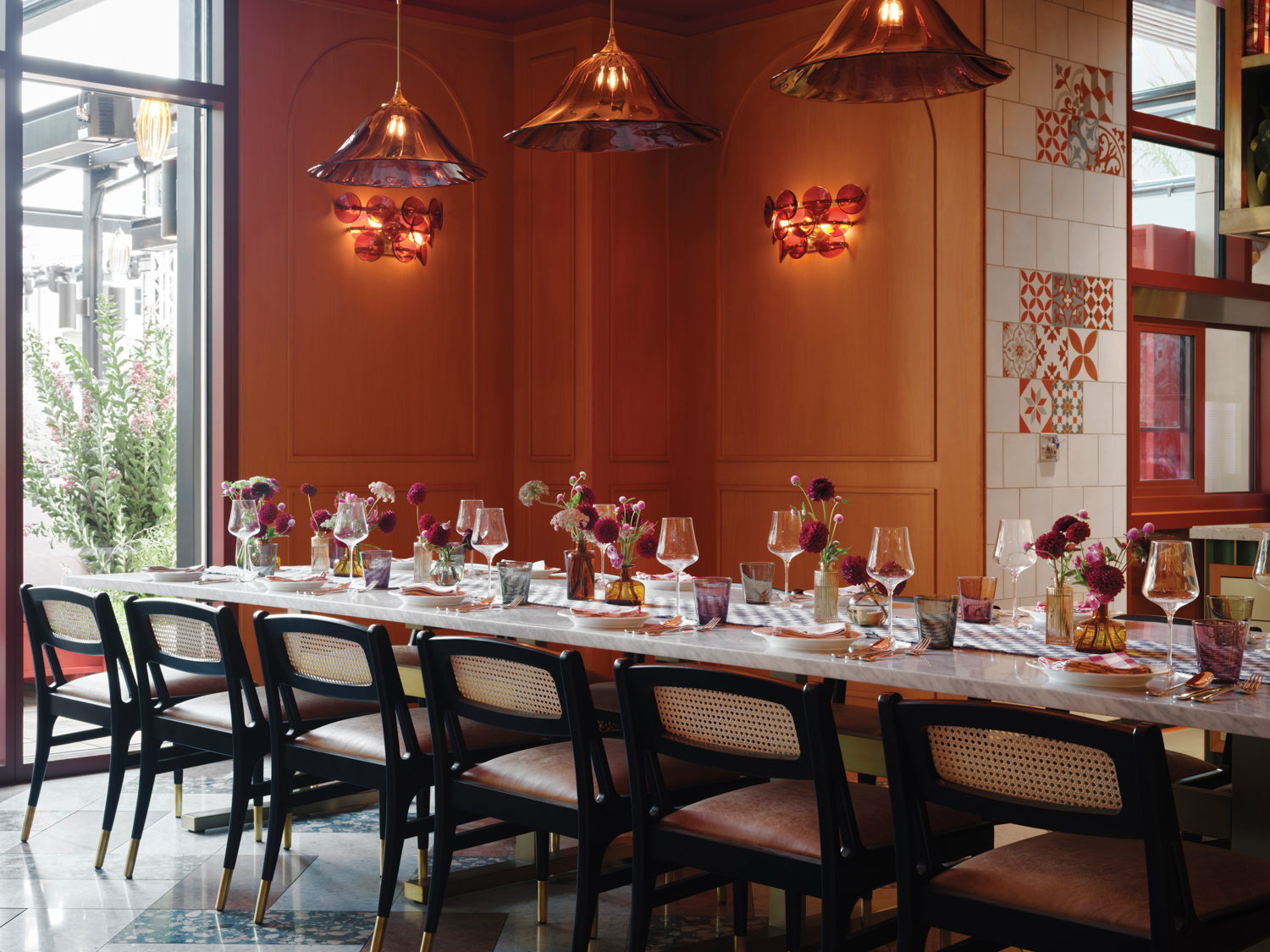 Long marble table and cane-back chairs with leather seats in a restaurant with wood-paneled walls