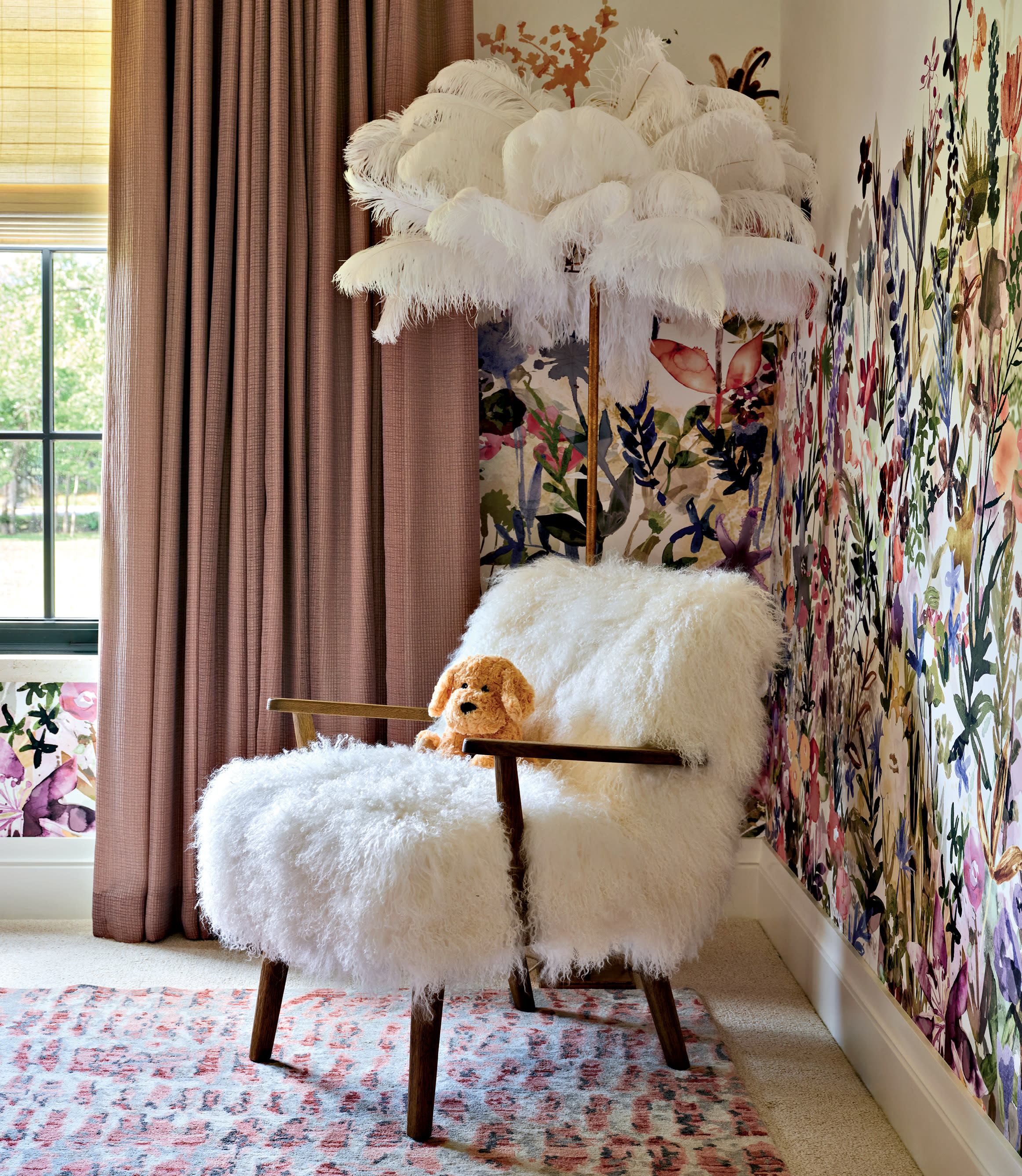 A cozy room features a fluffy white chair with a plush dog toy, under a feathered lamp. Vibrant floral wallpaper and muted curtains add warmth.