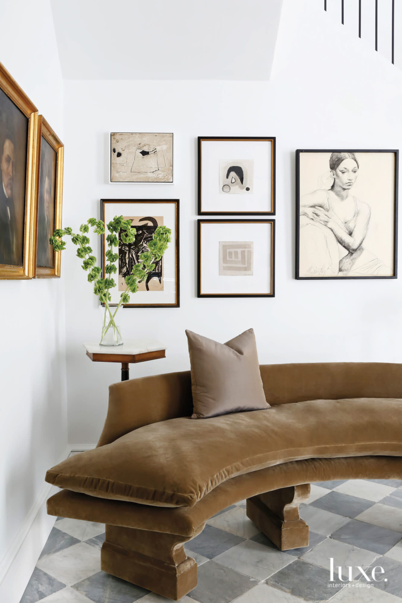 The corner of a white room with a curved brown bench, collage of wall art and gray-and-white checkerboard floors