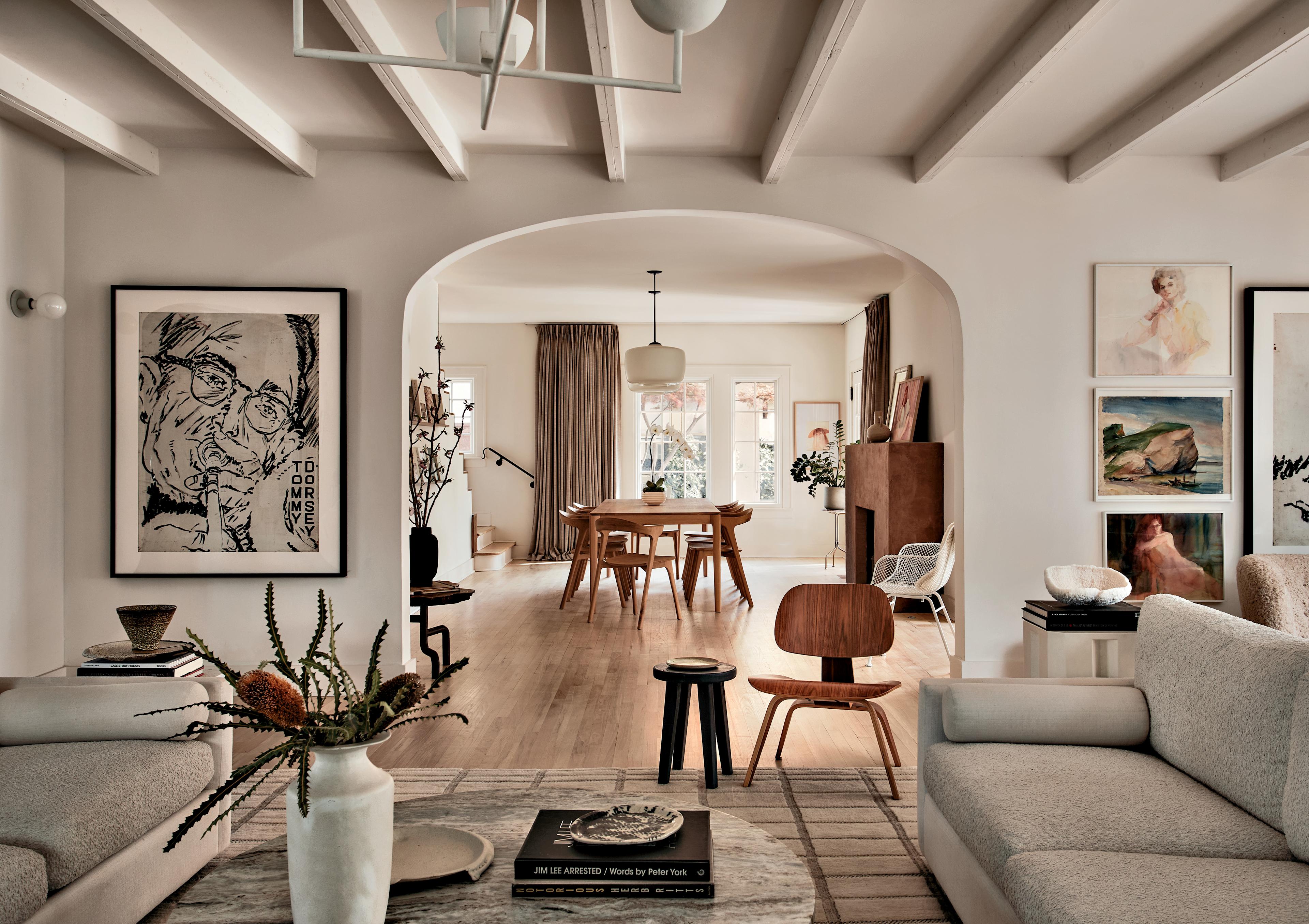 A walnut chair sits atop a rug near two sofas, with artwork on either side of an arched doorway.