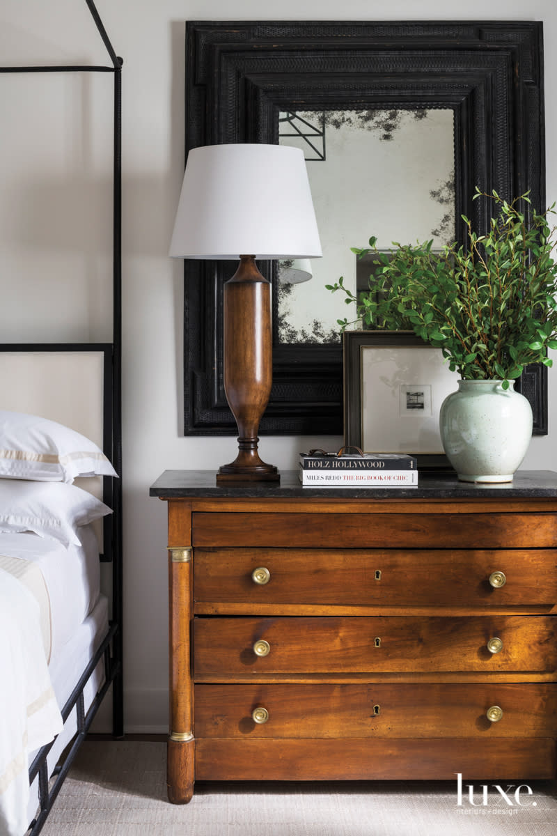 wood commode next to the bed in the master bedroom featuring a large mirror, lamp and plant