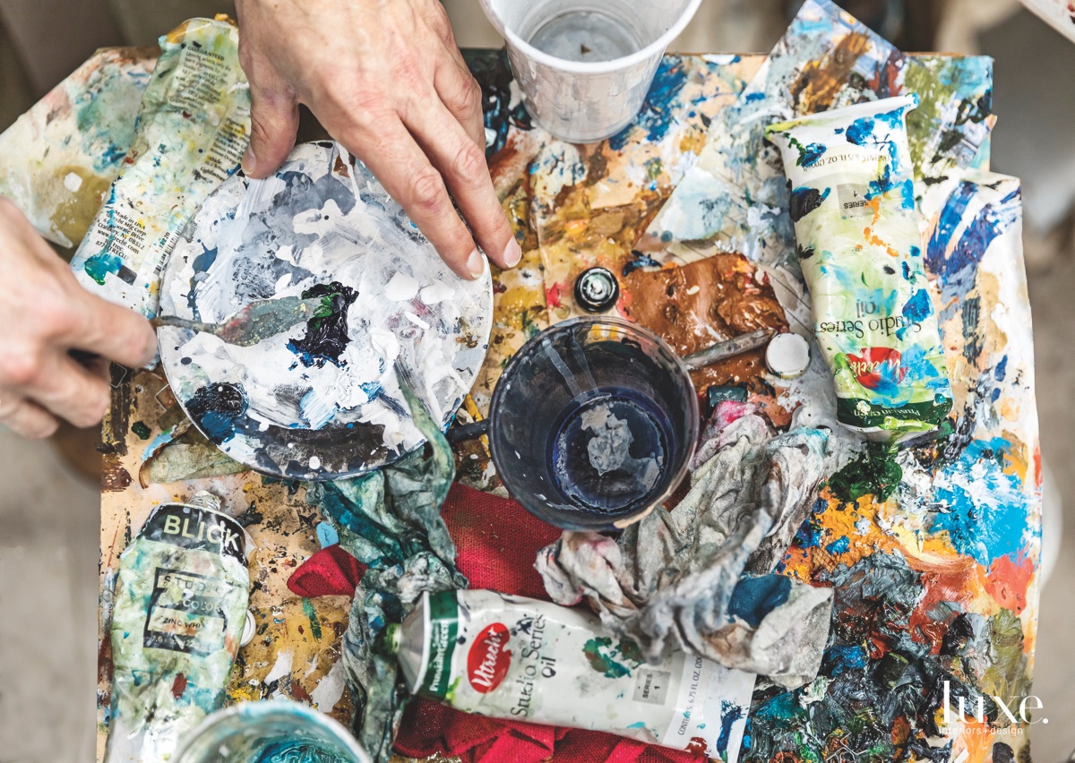 The artist's work space includes a large table-turned-palette--covered in paint tubes, oils, turpenoid, plates and more--where he mixes his paints