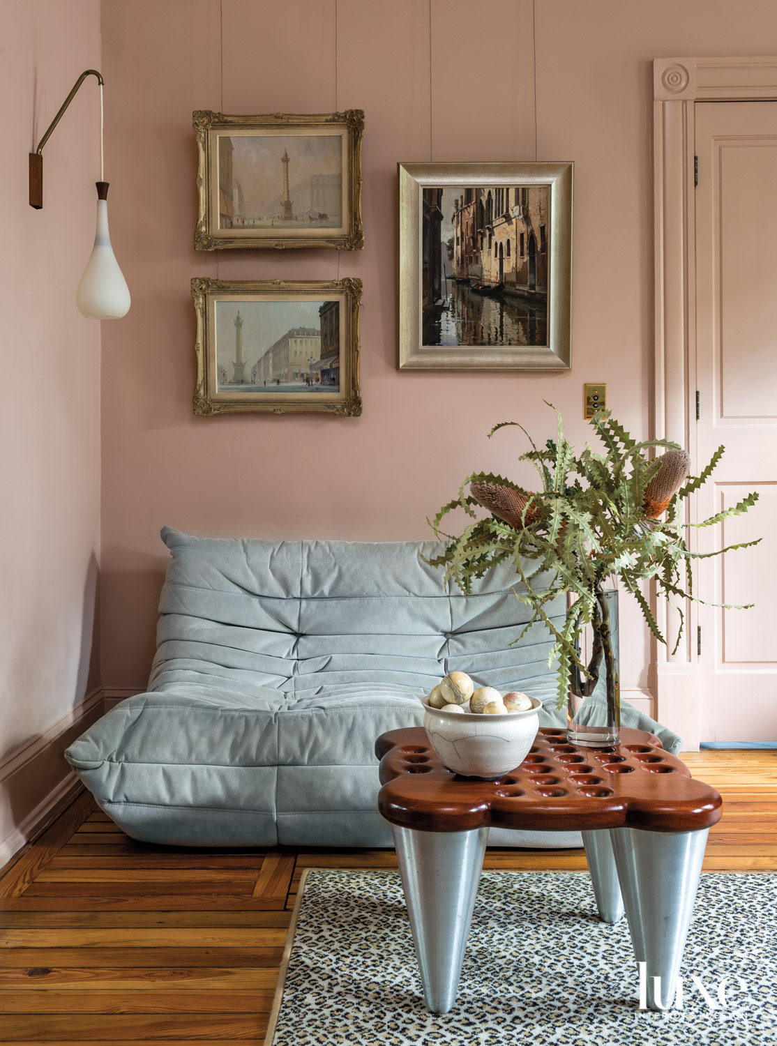 Sitting nook with blush-colored walls and millwork, pale blue lounge chair and framed scenic paintings