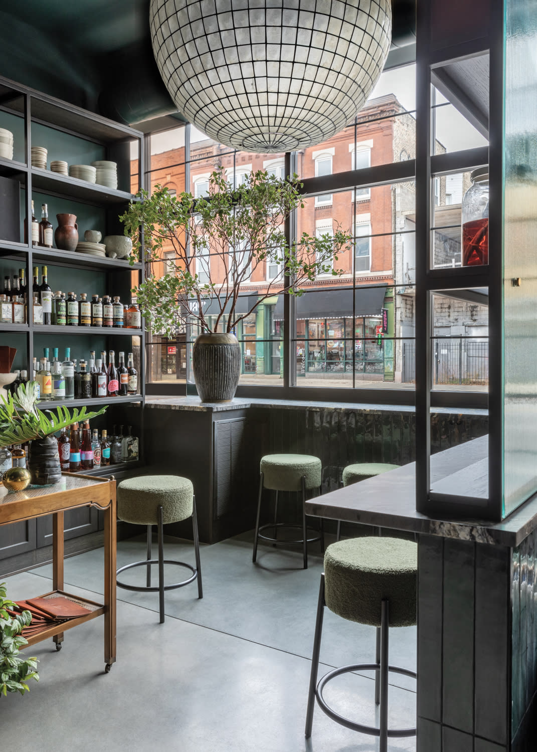 Market area of a restaurant with shelving filled with bottles and a large spherical light fixture