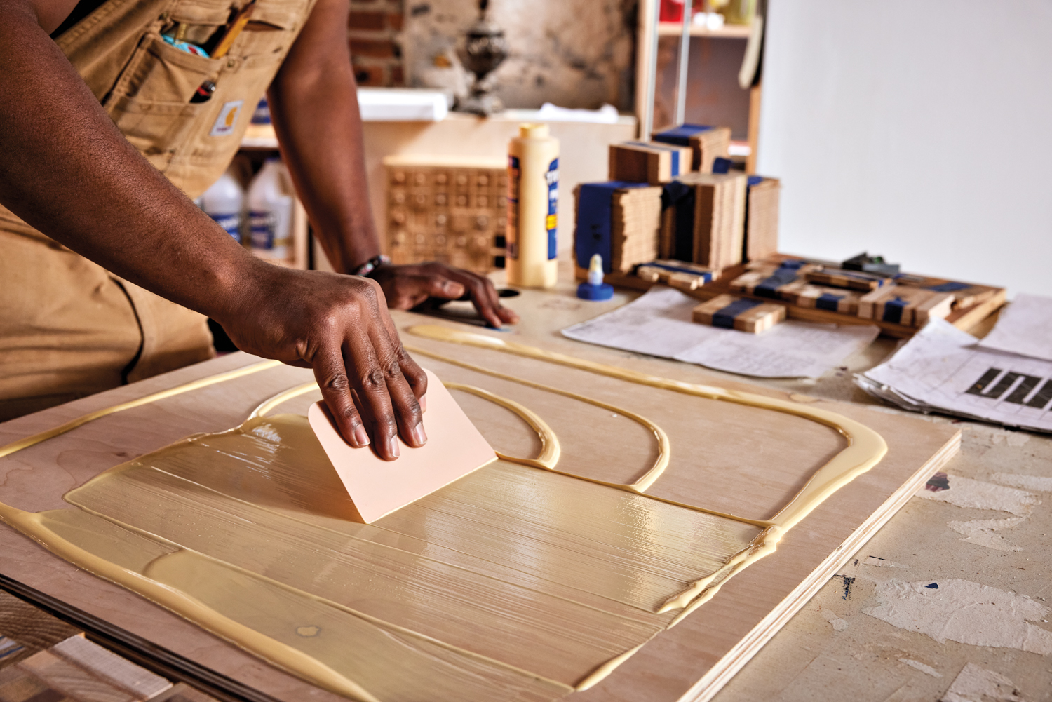 a man's hand spreading glue across a small wooden panel