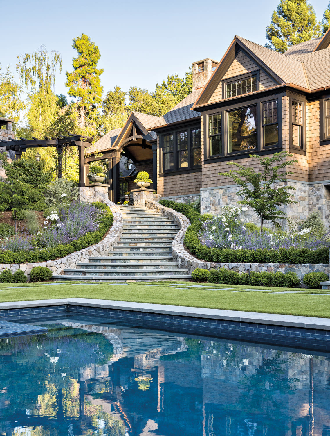 A large swimming pool is situated in front of a modern house, surrounded by a well-maintained lawn.