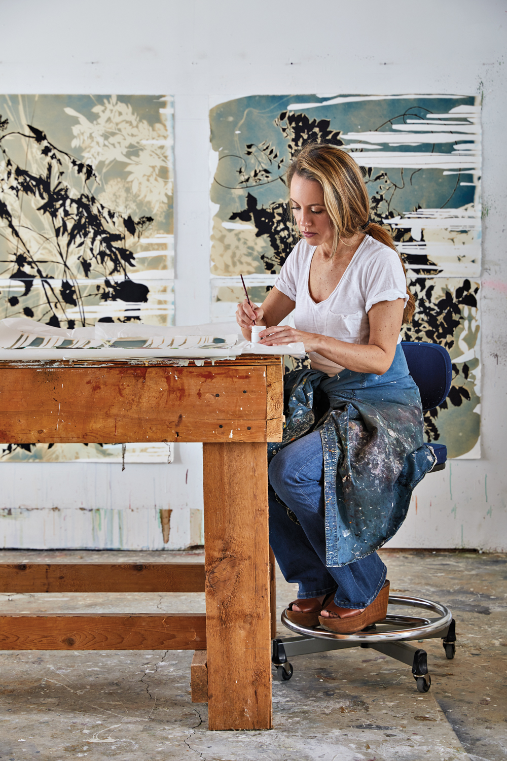 Woman working at a table with large artworks attached to the wall behind her