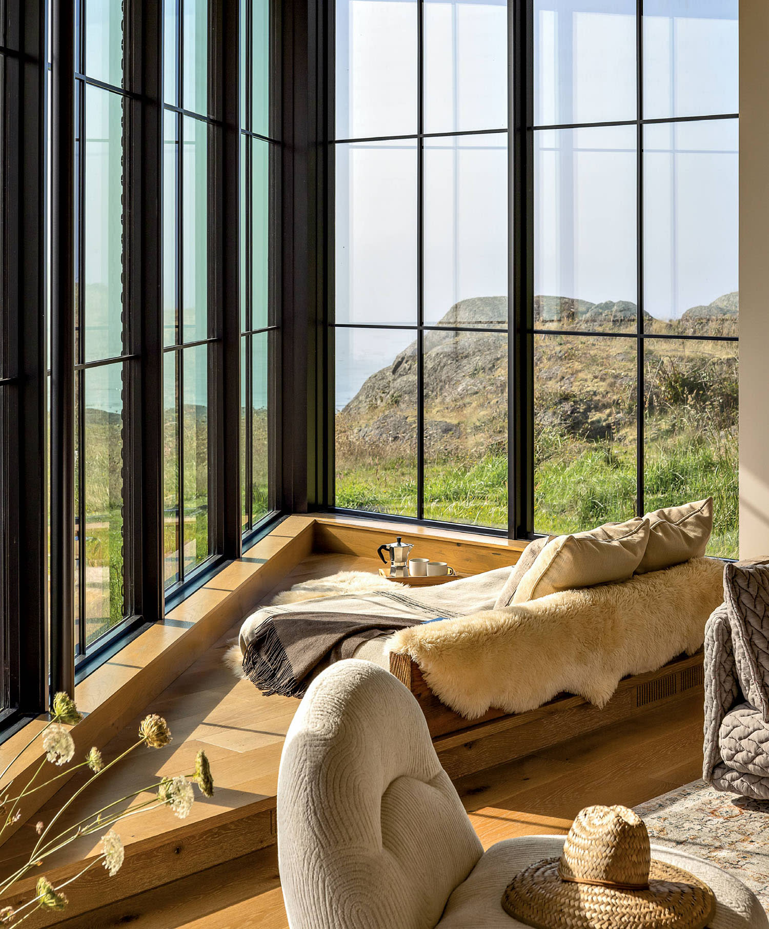A cozy corner of a living room near large windows with a sitting area and throw blanket.