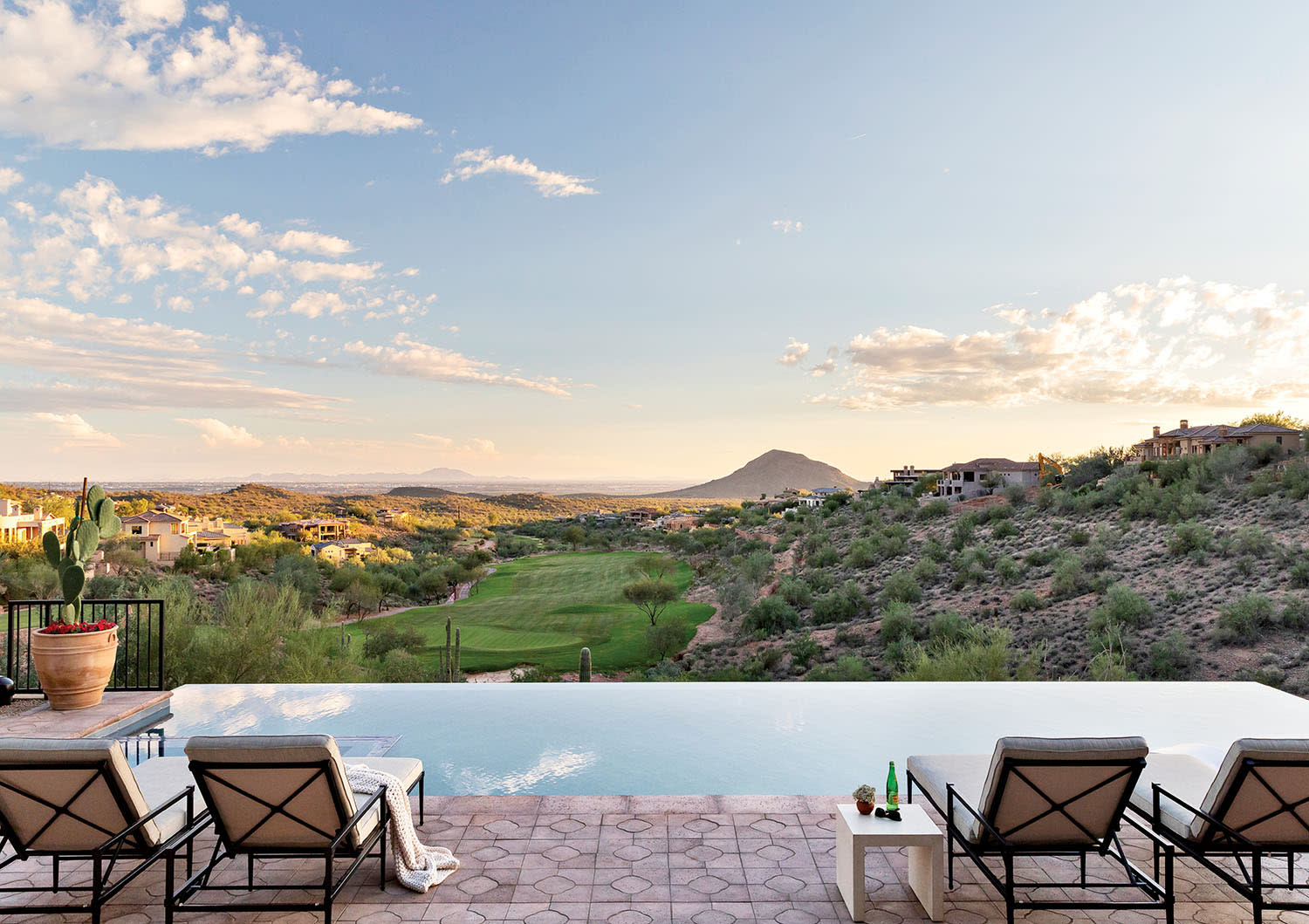 Infinity pool with sun loungers overlooking a scenic desert valley and distant mountains during sunset. The atmosphere is calm and luxurious.