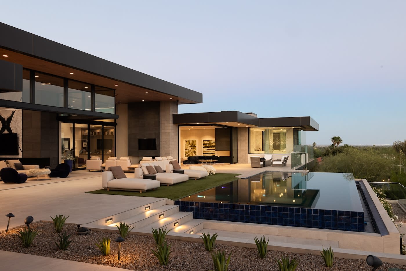 Modern luxury home with sleek architecture, featuring an infinity pool, outdoor seating, and warm lighting at dusk. Tranquil, upscale ambiance.