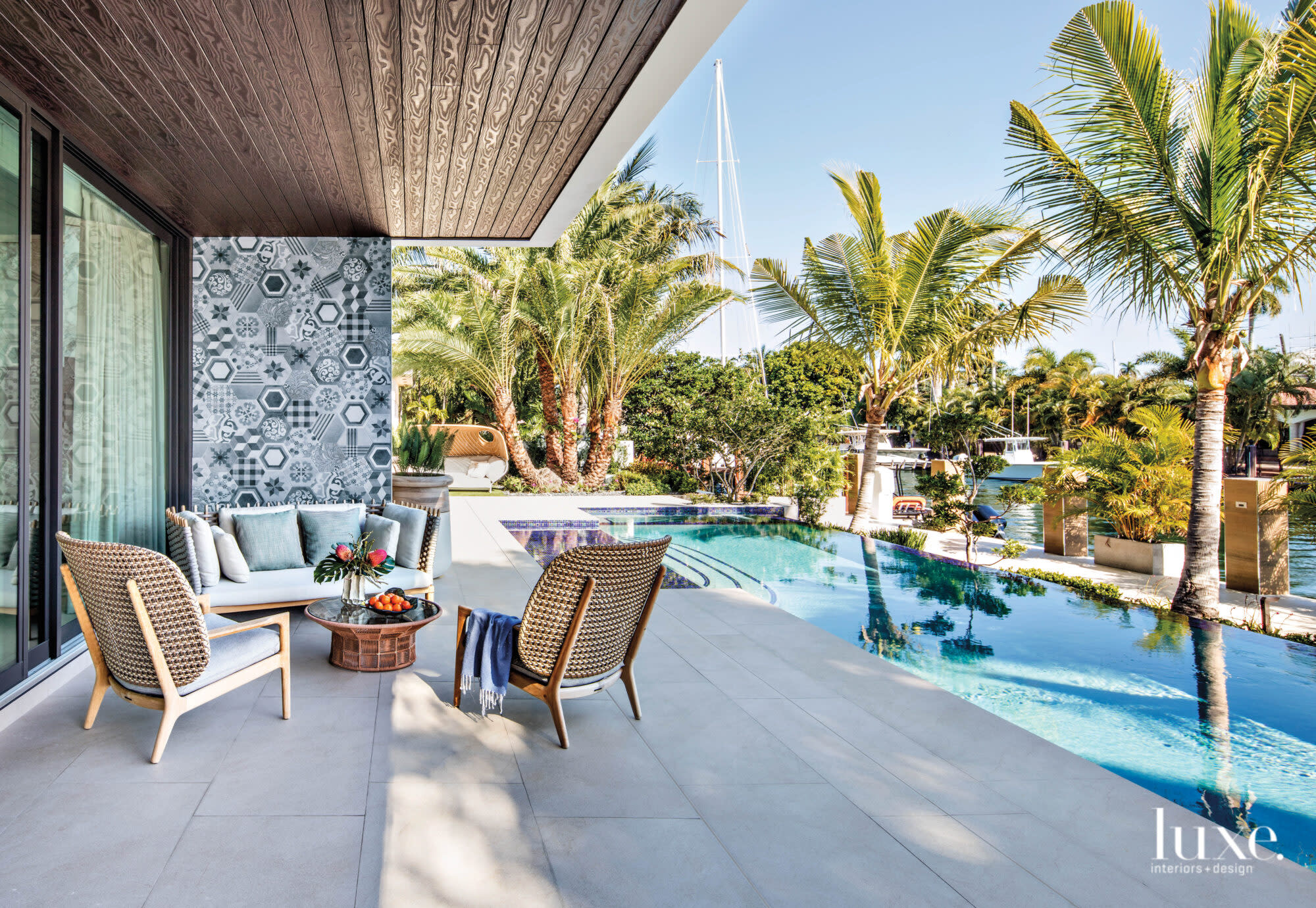 Covered seating area with teak chairs by pool.