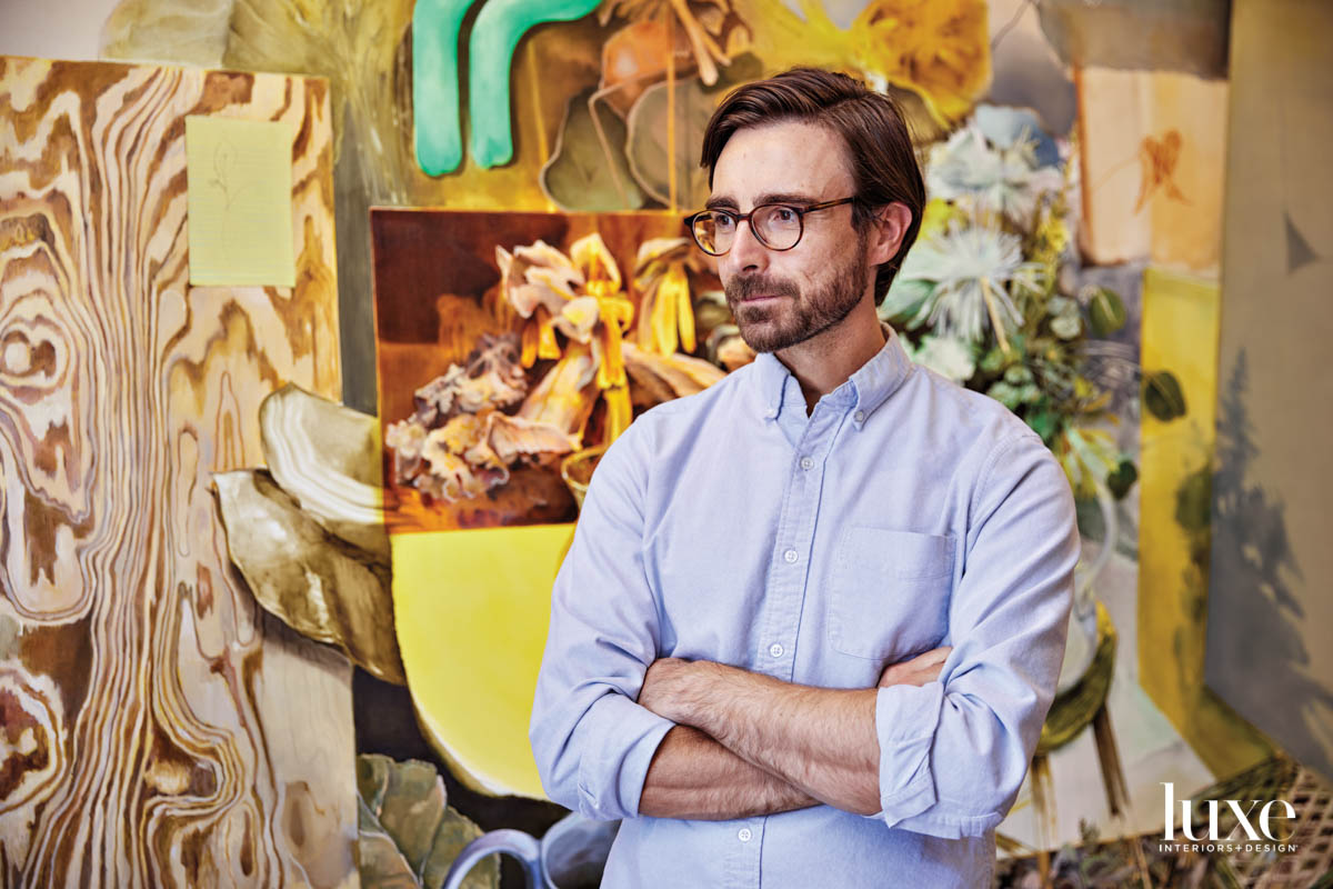 A man standing with his arms folded in front of a painting.