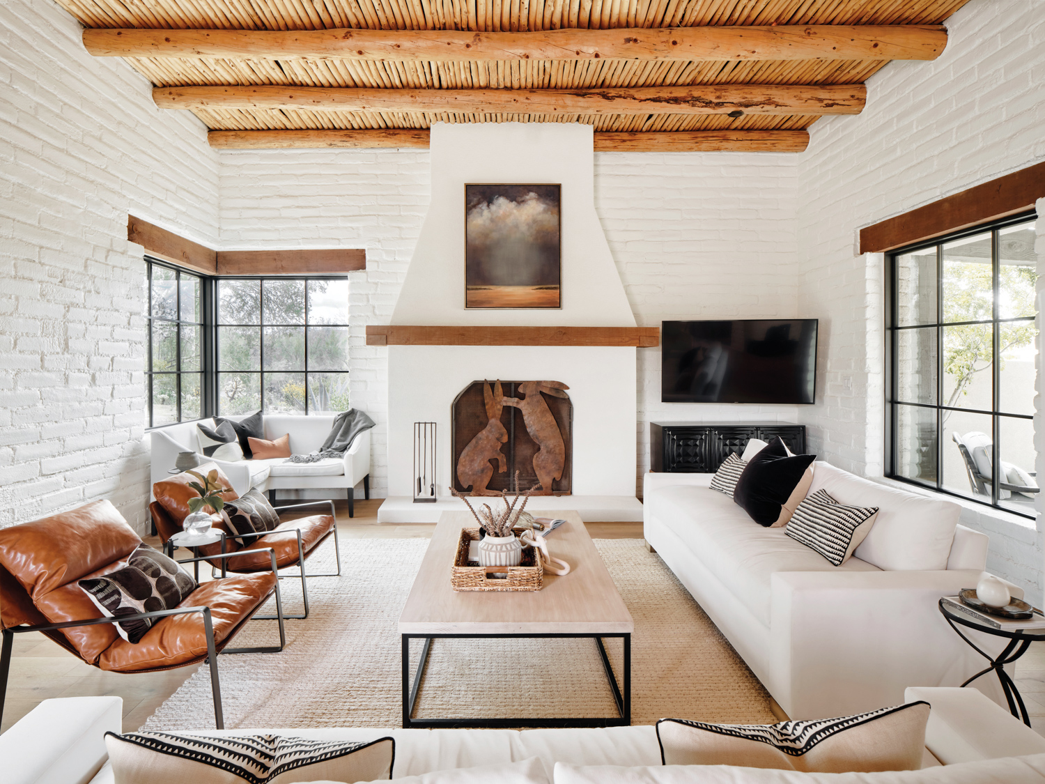 A living room with white brick walls, two brown leather armchairs and a white couch. The fireplaces has a decorative bunny screen.