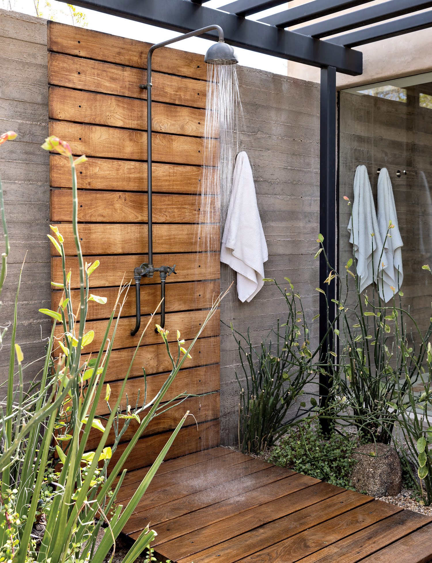 outdoor shower with a teak plank wall beneath a blackened-steel trellis