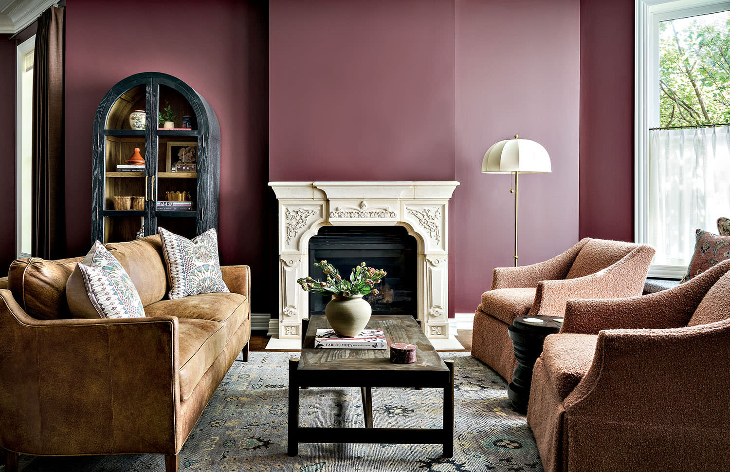 A living room with deep pink walls and a white stone fireplace, decorated with a couch and armchairs.