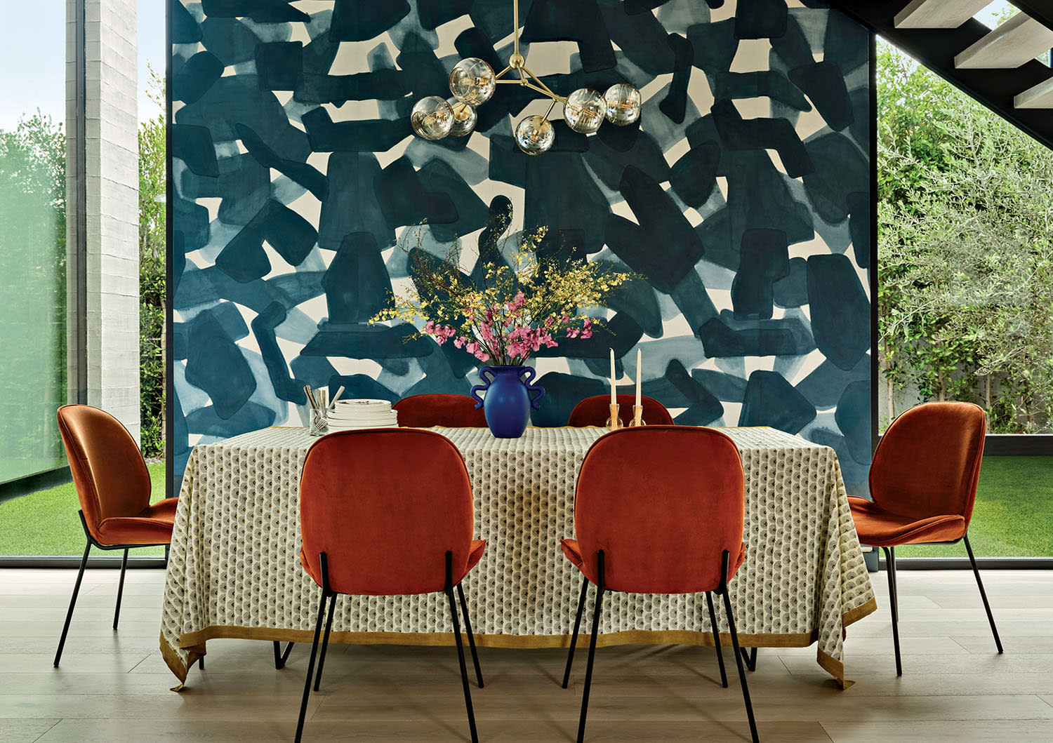 A modern dining room with six red velvet chairs around a table covered with a patterned cloth.