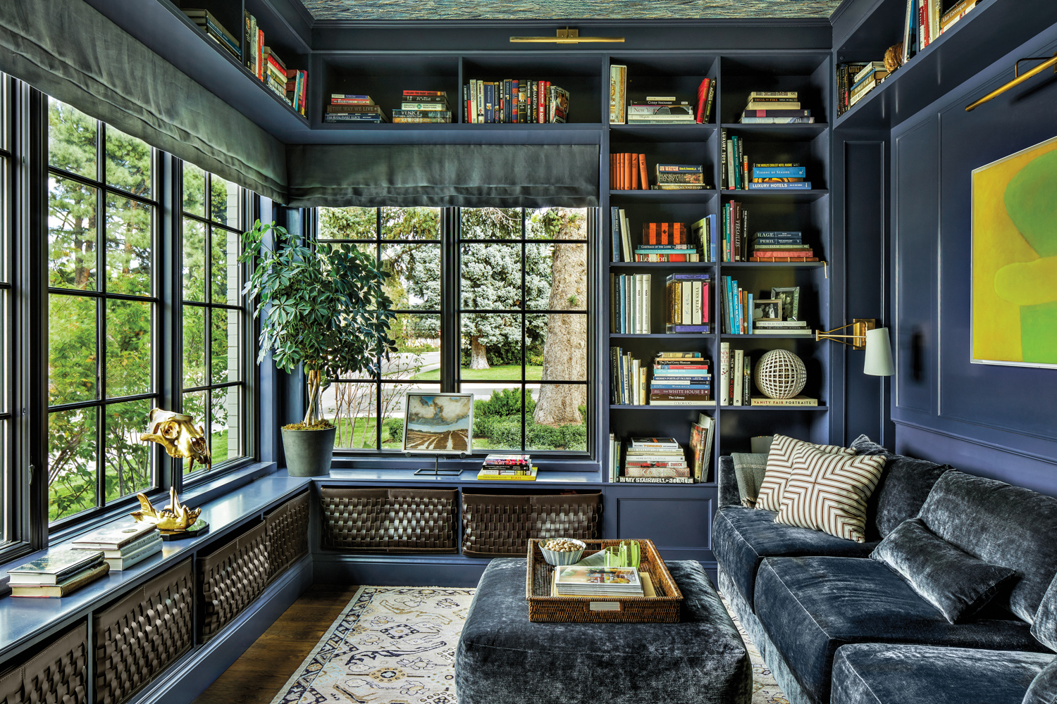 A library with blue built-in shelving, large windows, and a matching blue sofa and ottoman