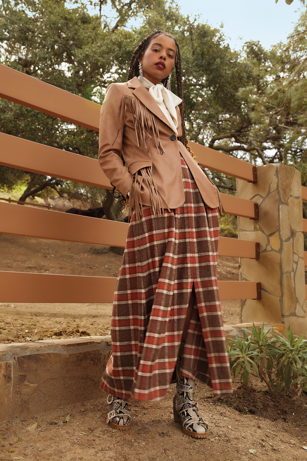 woman in front of fence in brown jacket and checkered skirt by Autumn Adeigbo