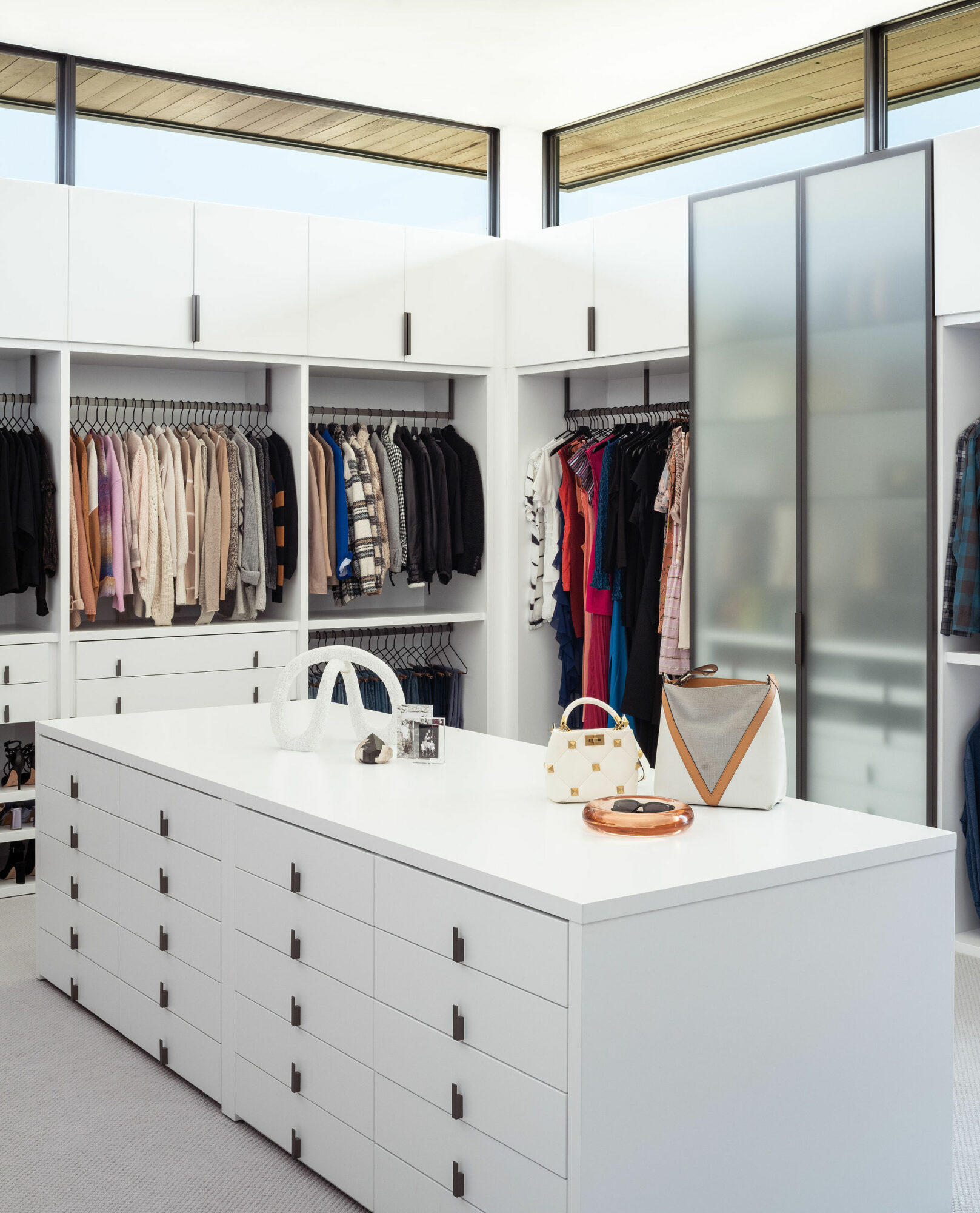 A well-organized walk-in closet filled with an abundance of clothes and accessories, featuring cabinets and an island.