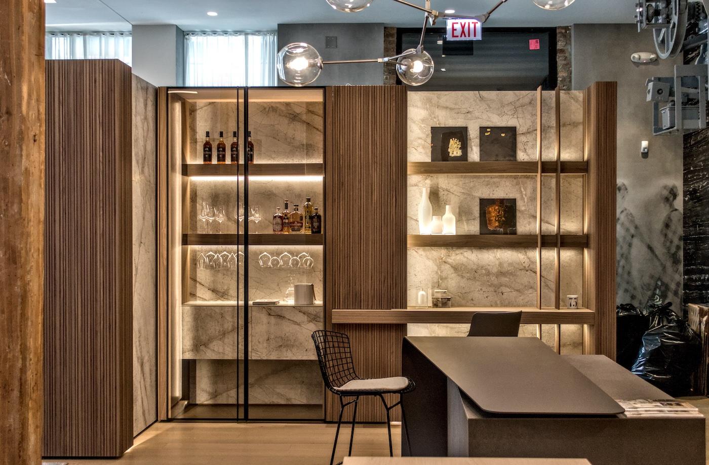 Modern lounge area with a marble and wood display unit featuring bottles, glasses, and decorative items. A sleek bar counter and chair add elegance.