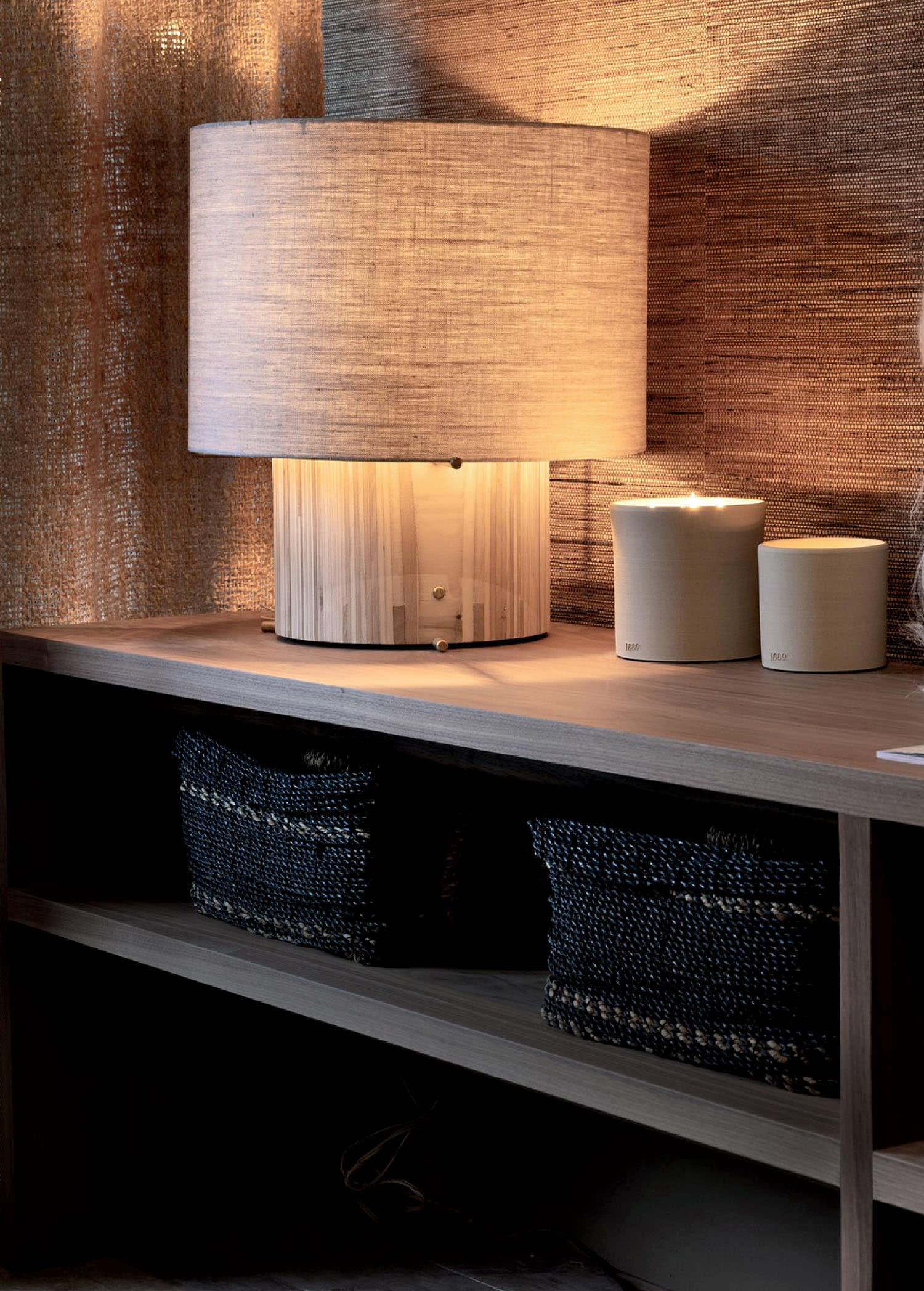 A lamp sits on a corner on a shelf next to candles.