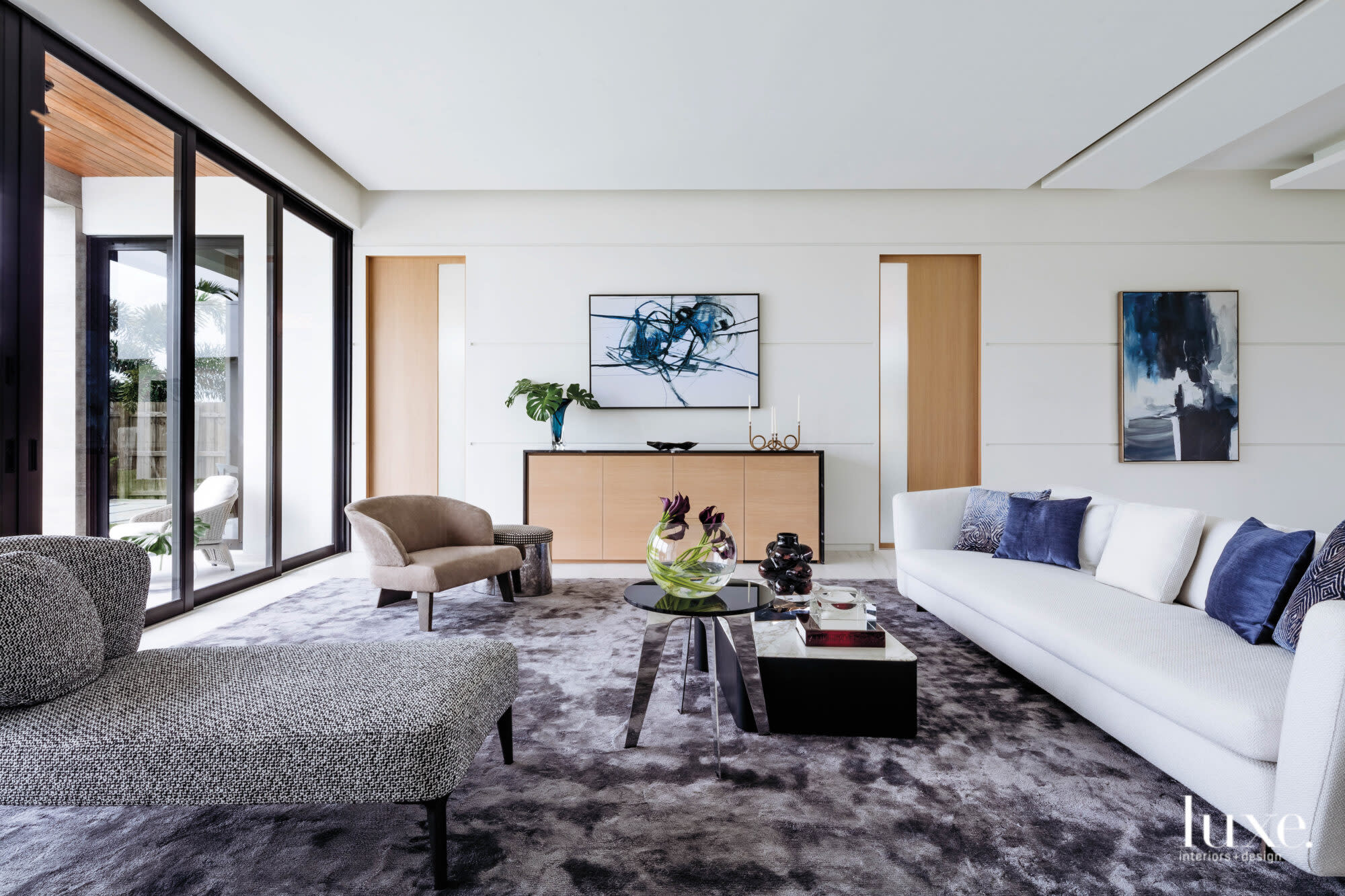 Neutral-tone living room with with blue pillows, purple tabletop decor and blue artwork.