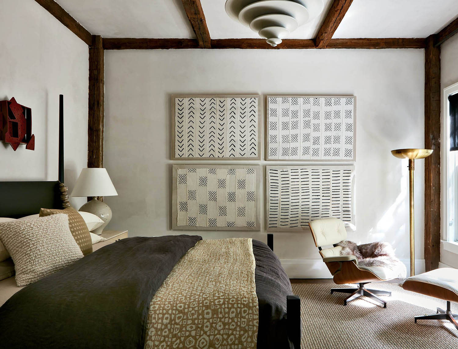 A quartet of geometric artwork on the wall in a bedroom with a bed, nightstand and seating area.