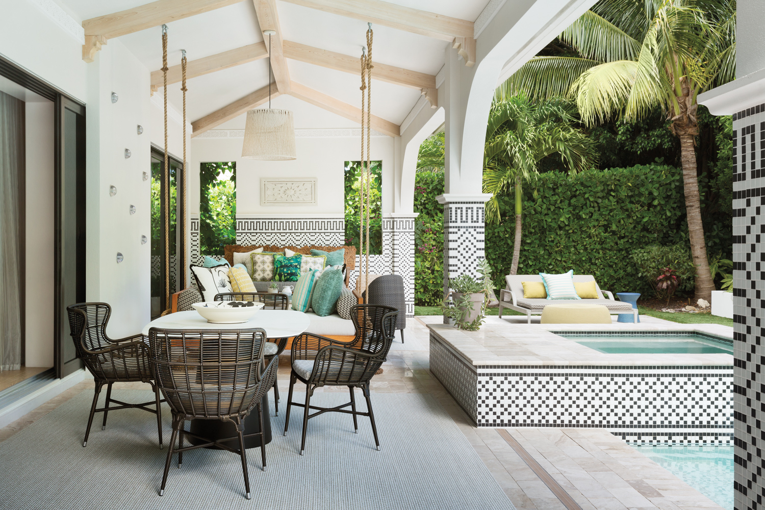 loggia with mosaic tiles, dining tables, black chairs, hanging daybed and pool