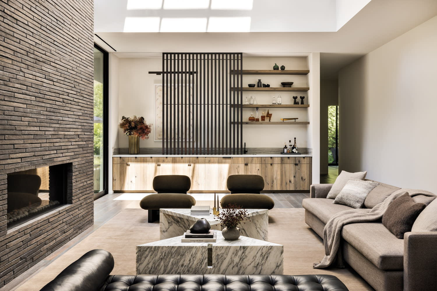 living room with marble coffee tables, black upholstered bench, green chairs, a sofa and a bar by Marmol Radziner