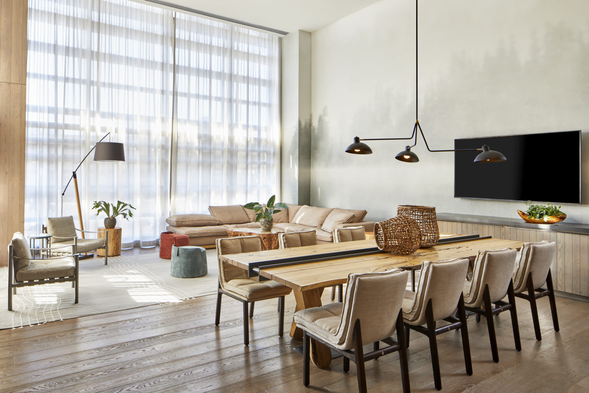 wall of floor-to-ceiling windows back an open layout living and dining area with a neutral palette