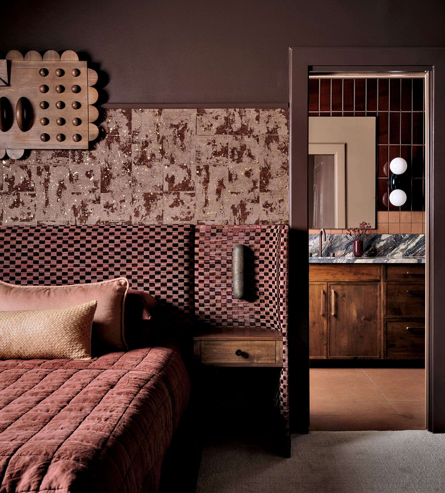 A bedroom with a checkered fabric headboard, patterned wallpaper and a quilt with coordinating pillows.