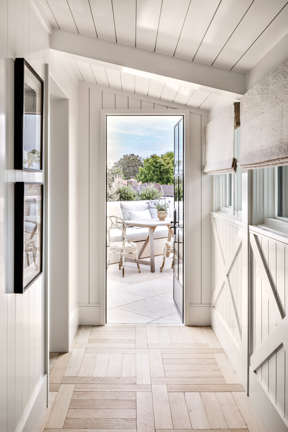 hallway lined with white shiplap leading to exterior patio area with table and chairs in home by Marie Carson