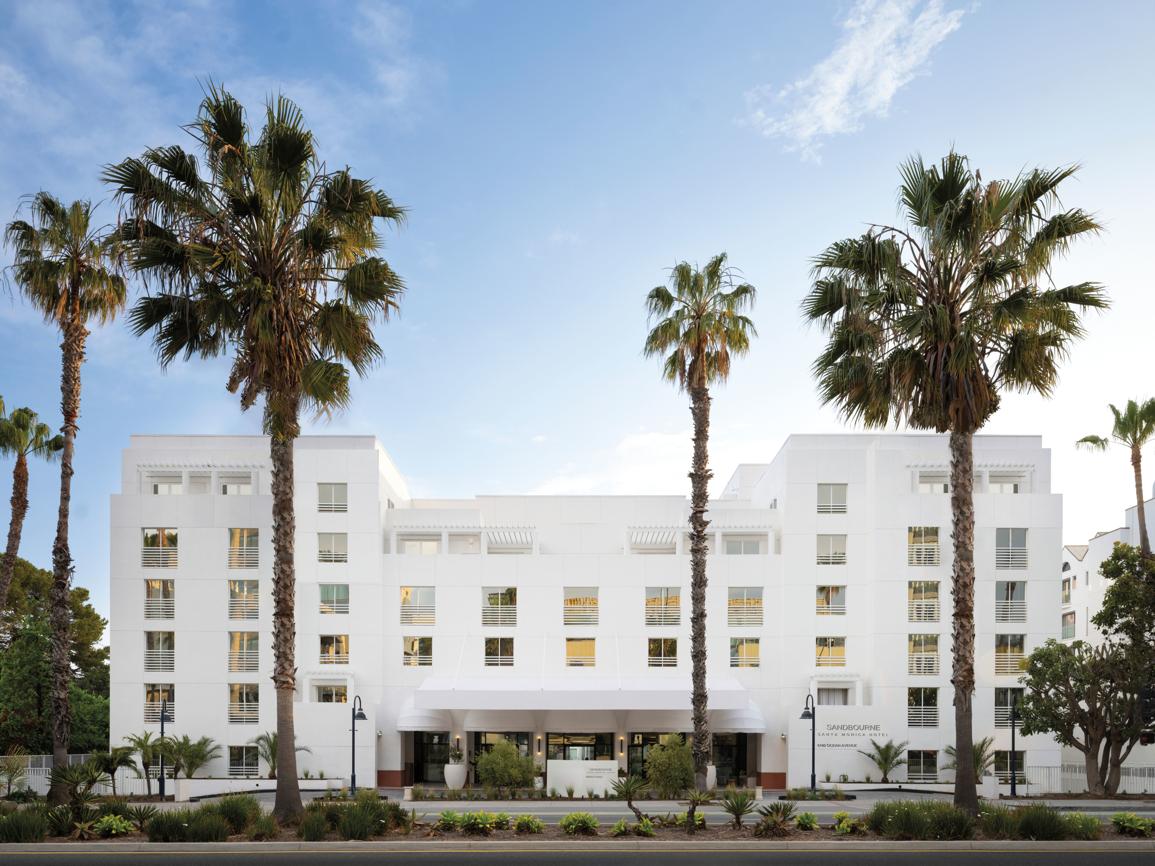 white exterior of the Sandbourne Santa Monica hotel with palm trees in front of it