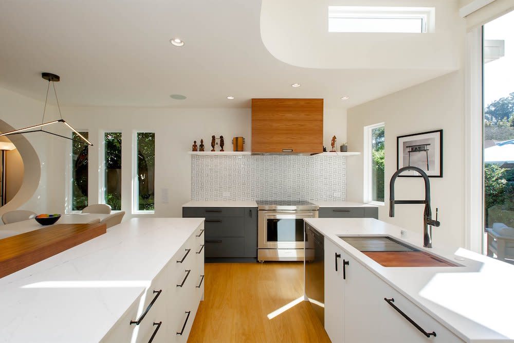 A kitchen with a clean and minimalist design. White cabinets and countertops create a bright and airy atmosphere, complemented by a light wood range that adds warmth to the space. The overall aesthetic is modern and inviting.