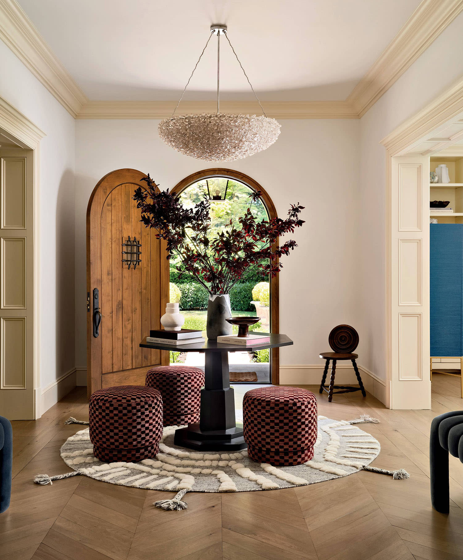 A table, trio of ottomans and a pendant light sit in an entryway on a circular rug by an open door.