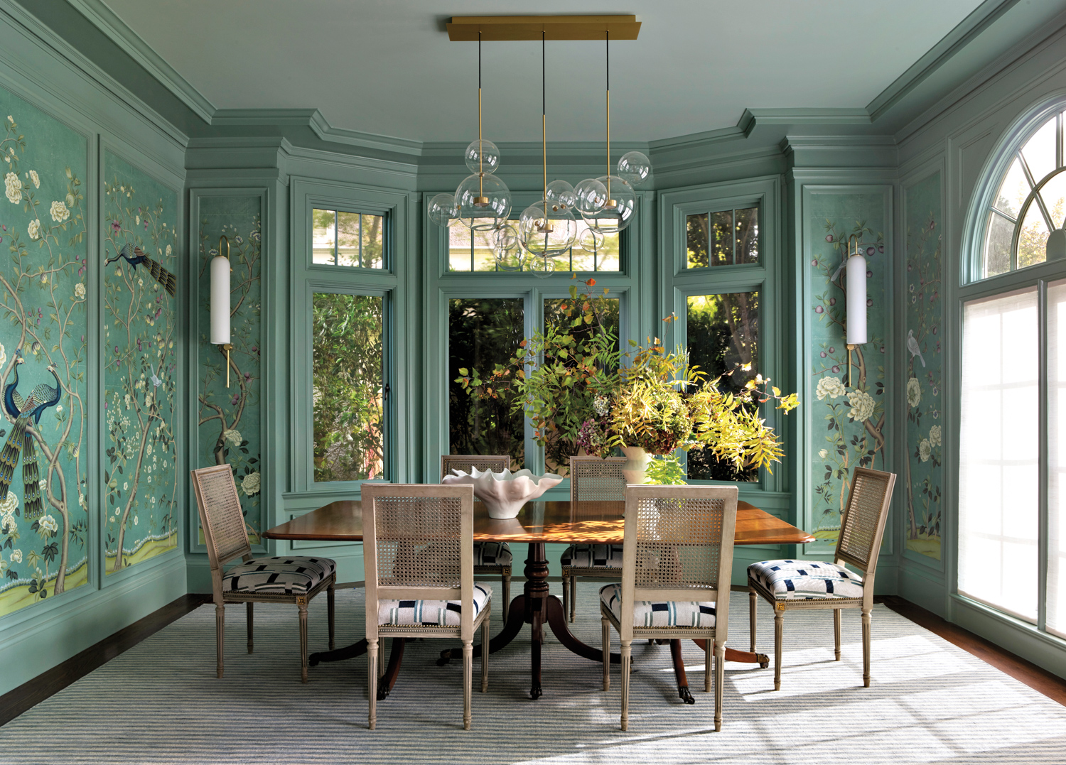 Dining room has green molding and paneled wallpaper, plus vintage chairs and an antique dining table