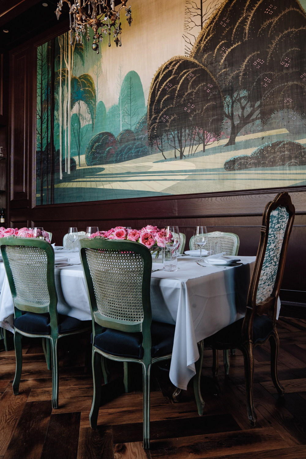 dining table with vintage chairs underneath a crystal chandelier and large-scale landscape mural