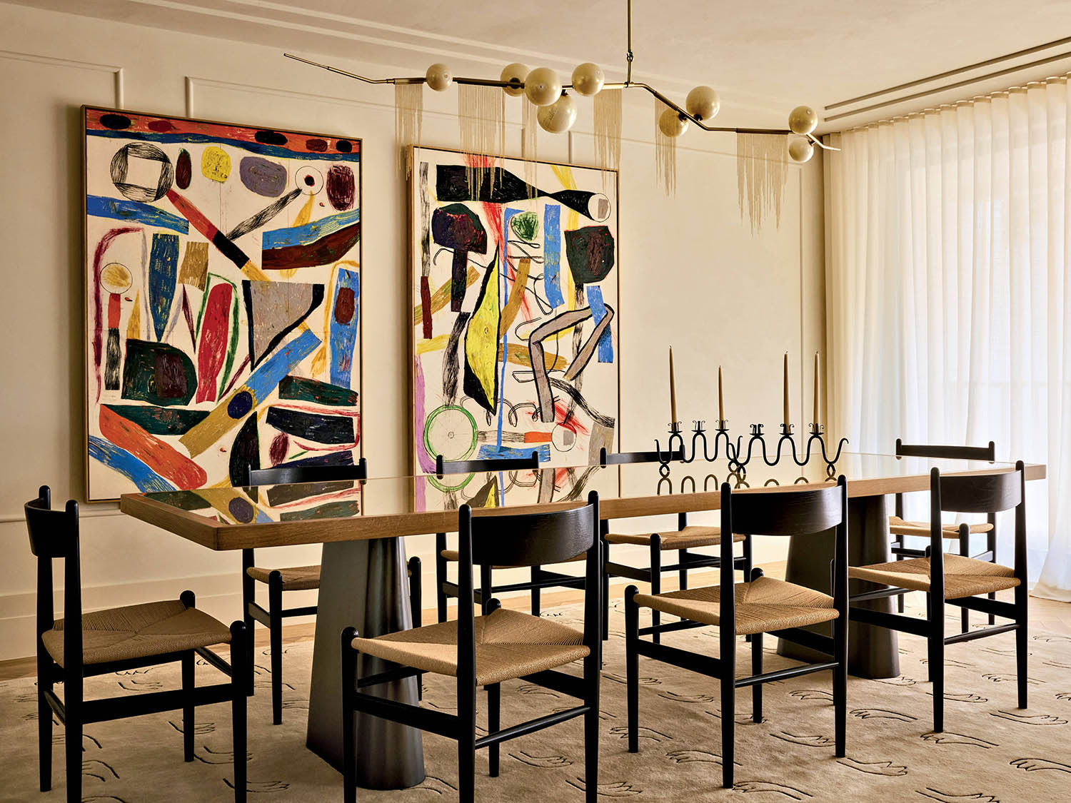 Two pieces of abstract art hang behind a dining table surrounded by chairs and sitting atop a rug.
