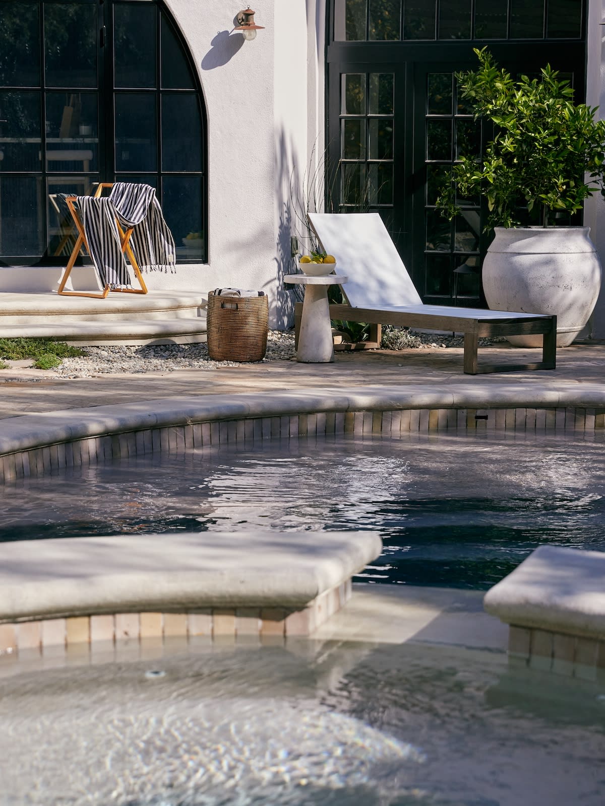 A serene poolside scene featuring a lounge chair and a small table beside the water.