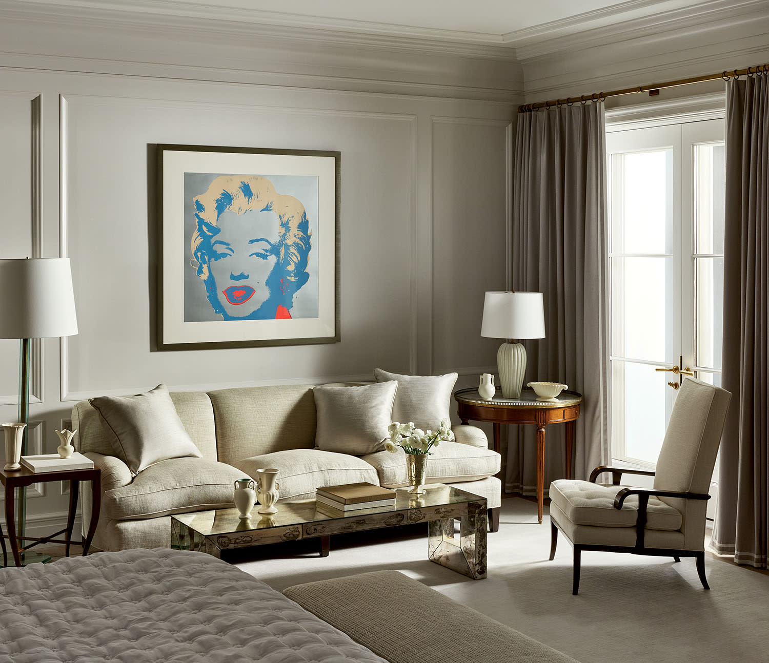 Elegant living room with a neutral palette features a large sofa, glass coffee table, and pop art portrait on the wall. Soft lighting and curtains create a cozy ambiance.