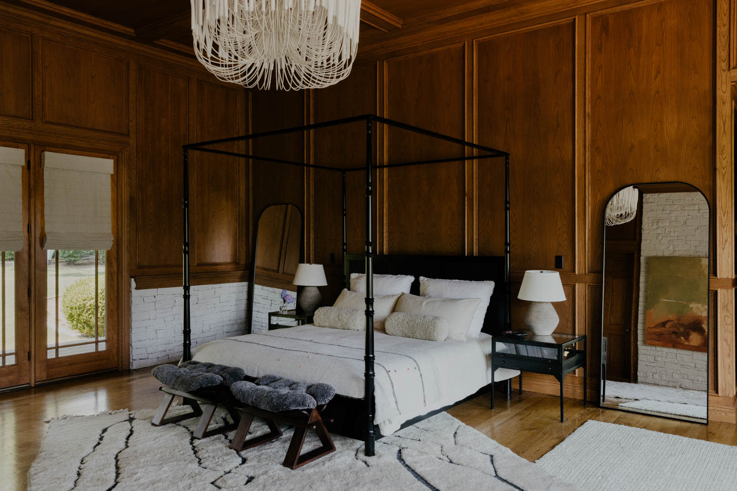 traditional bedroom with a black four-poster bed, wood paneled walls and a white chandelier