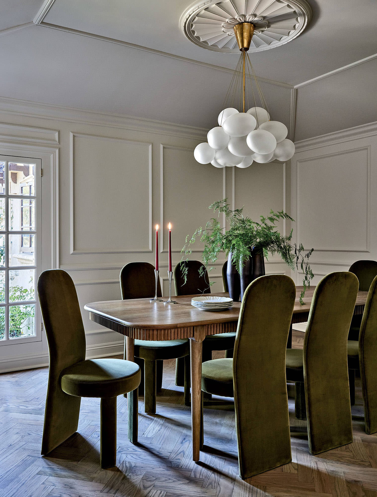 A wood dining room table sits in with a chandelier above and French doors leading to an outdoor area.