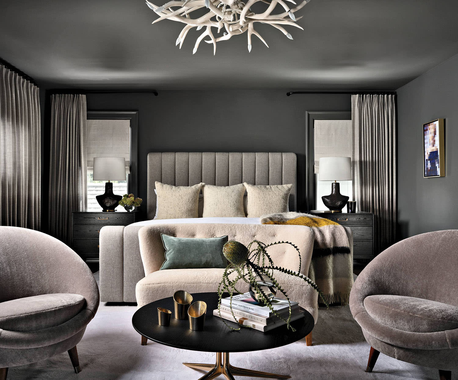 moody bedroom with gray color-drenching beneath an antler chandelier