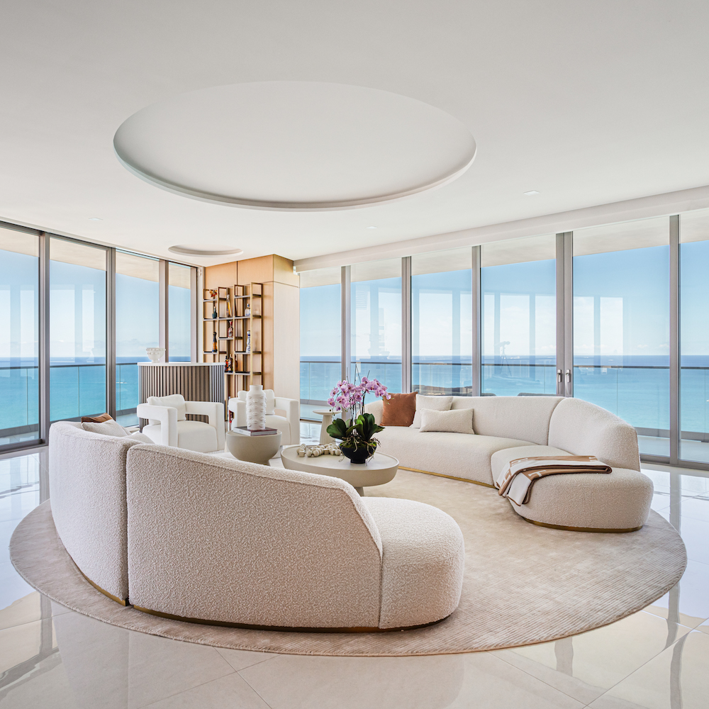 Bright living room with a circular couch, offering a beautiful view of the ocean through expansive glass doors.