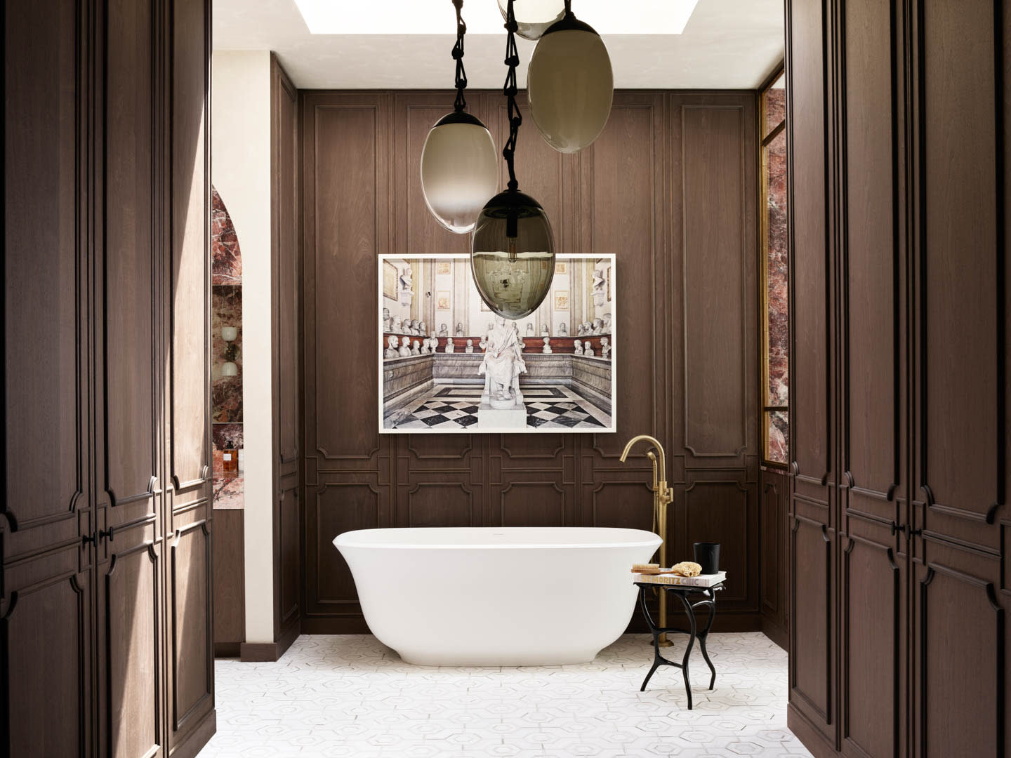 Luxurious bathroom with dark wood paneling, a freestanding white tub, and elegant pendant lights. A classical art piece hangs behind the tub, creating an opulent feel.