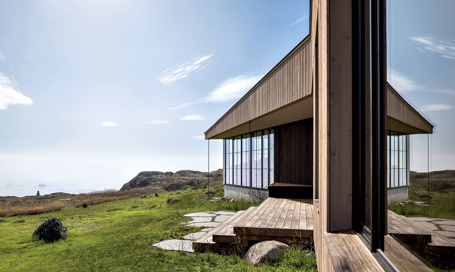 A home on a waterfront hill with a wood-paneled exterior, stairs and large front windows.