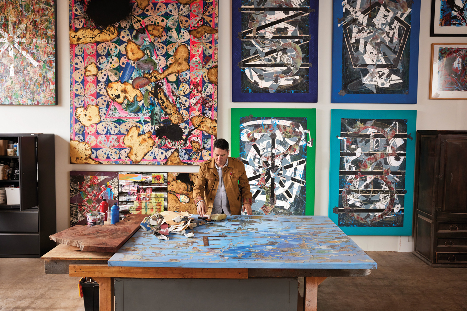 a man painting with large colorful paintings hanging on the wall behind him