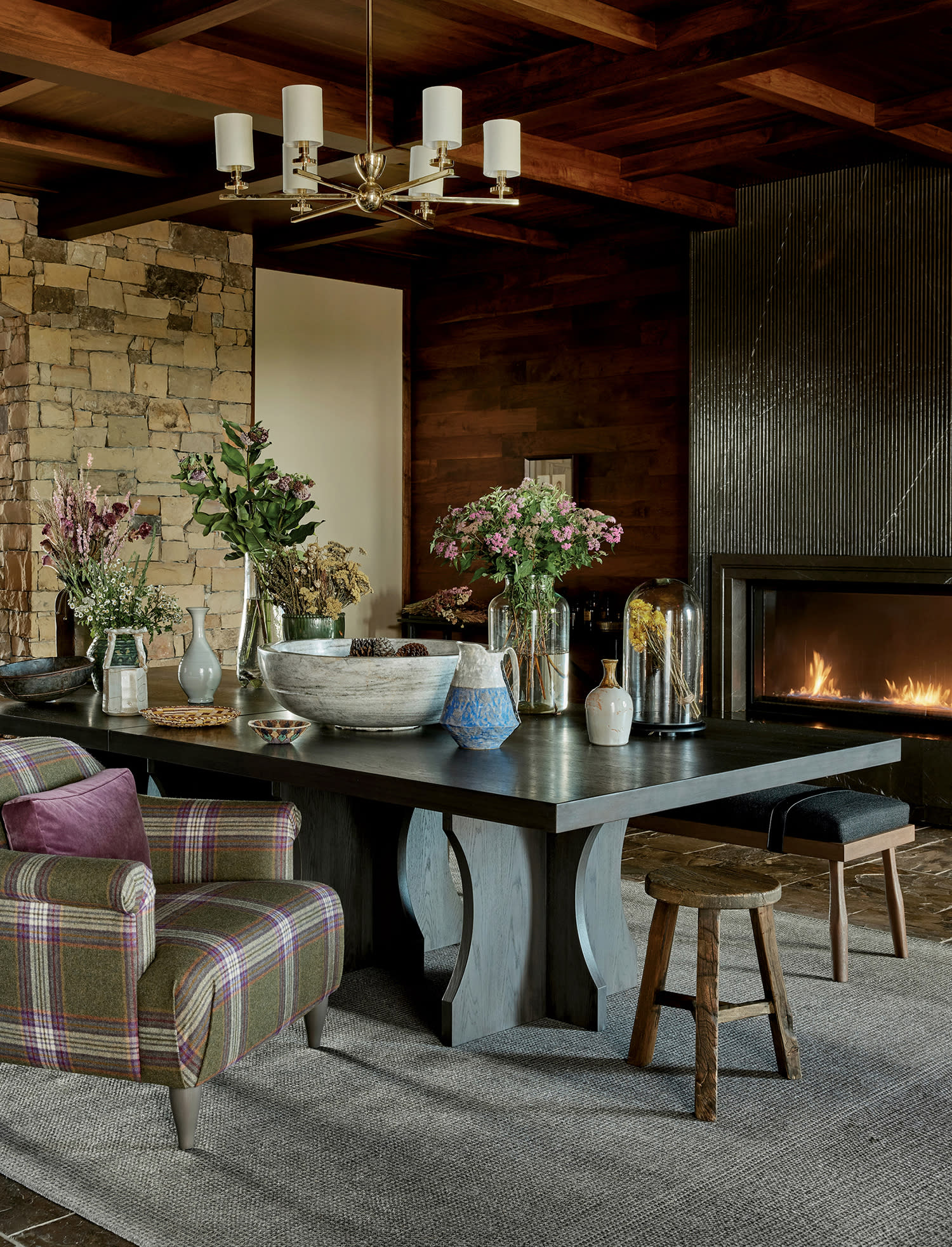 Warm lodge interior with a stone fireplace, wood ceiling, floral accents and plaid seating
