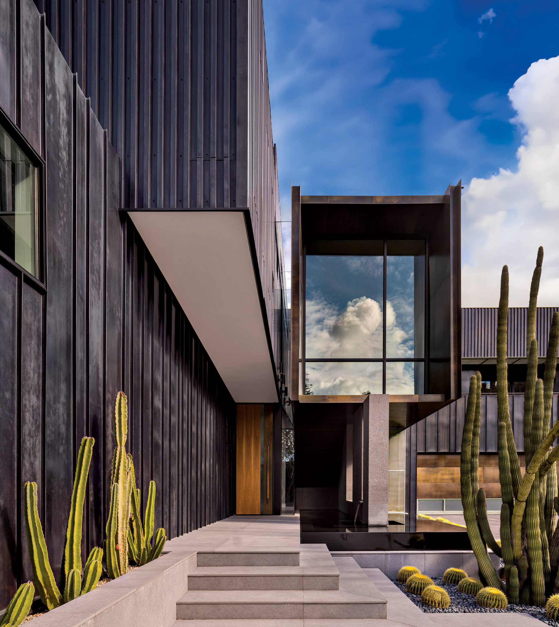 Blackened-copper paneling lines the exterior of an Arizona home with cacti along the entry